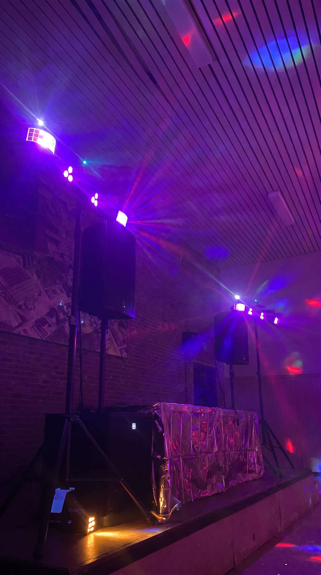 DJ-booth op een podium met speakers op statief en paarse lichtbars in een feestzaal